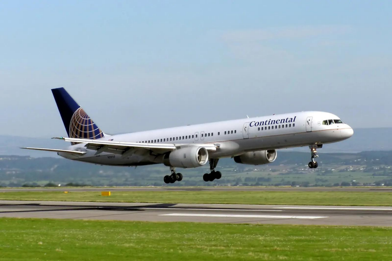 A Continental Airlines passenger airplane is landing on a runway with landscape in the background.