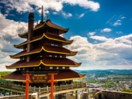 A multi-story pagoda stands on a hilltop overlooking a cityscape and greenery, with a sign reading "The Pagoda, City of Reading" in the foreground. Clouds dot the sky above.