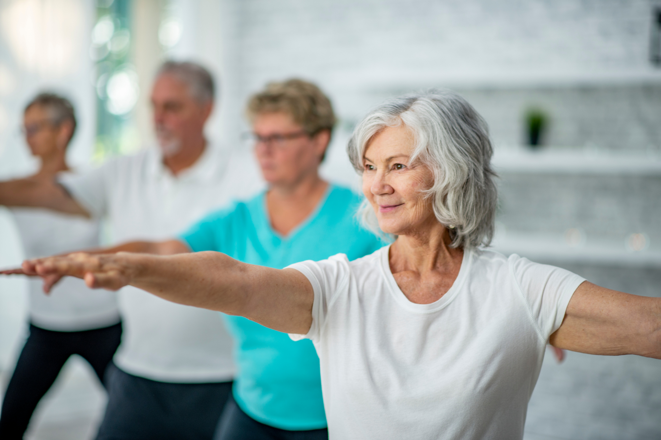 A group of four older adults performs yoga poses in a bright, indoor studio, focusing intently.