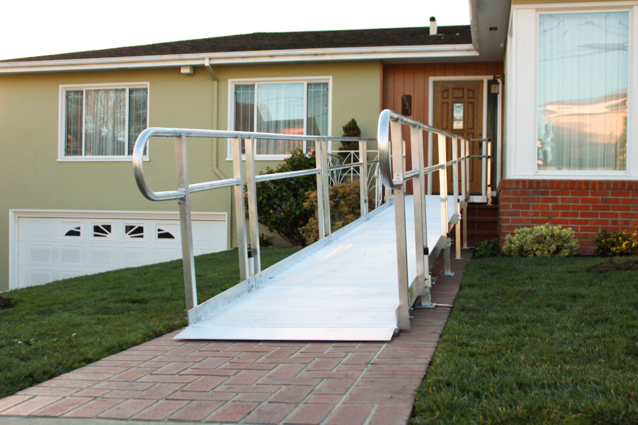 Aluminum wheelchair ramp installed at the front entrance of a house, leading from the sidewalk to the front door.