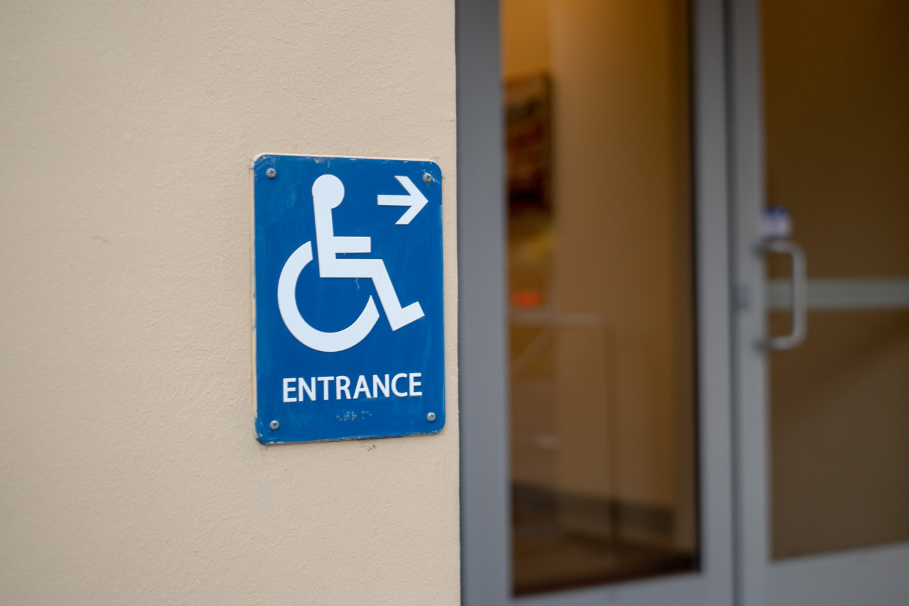 Blue sign with a white wheelchair icon and the word "ENTRANCE" points toward a door in the background.