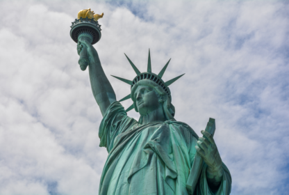 A close-up view of the Statue of Liberty against a cloudy sky, showing the torch in her raised right hand and a tablet in her left.