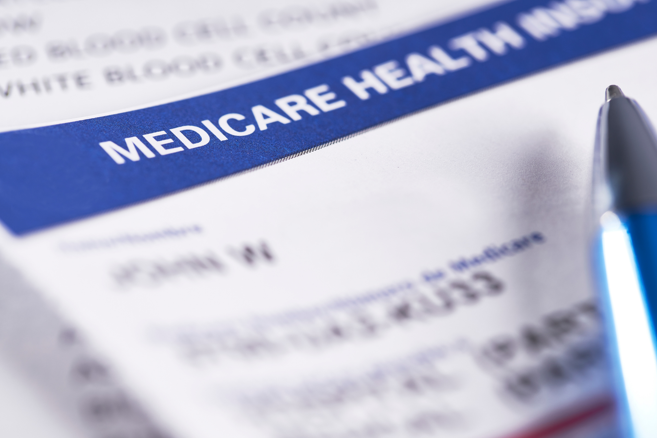 Close-up of a Medicare health insurance card with a pen placed on top of the document. The card includes text and personal information relevant to healthcare coverage.