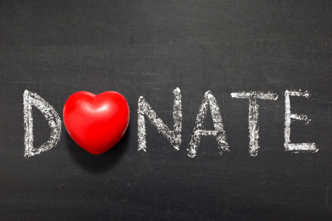 Chalkboard with the word "DONATE" written in white, where the letter "O" is replaced by a red heart-shaped object.