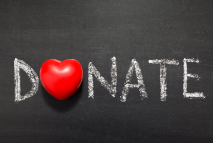 Chalkboard with the word "DONATE" written in white, where the letter "O" is replaced by a red heart-shaped object.