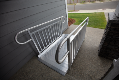 A metal wheelchair ramp installed on a concrete doorstep, providing accessibility to a building with gray siding.