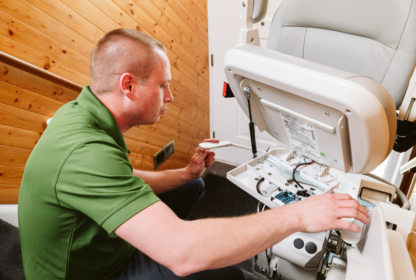 A technician in a green shirt is repairing a stair lift, focusing on its electronic components.