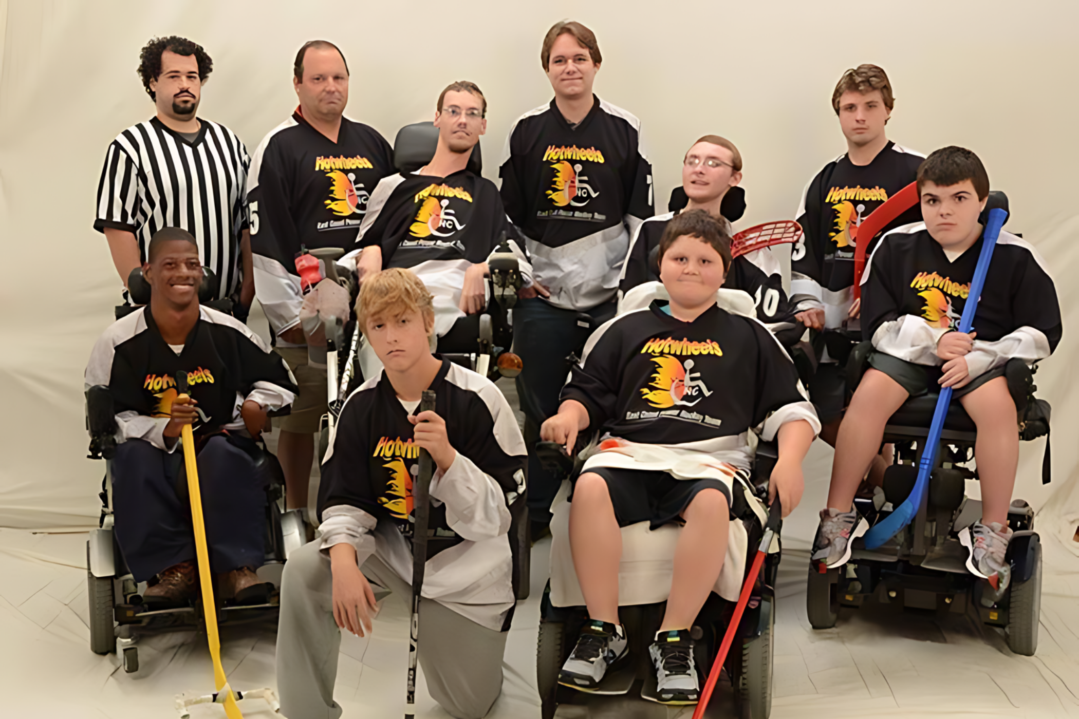 A mixed group of nine people, some in wheelchairs, dressed in sports uniforms with a referee standing beside them. They appear to be a team posing for a group photo.