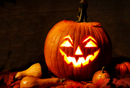 A glowing jack-o'-lantern with a carved smiling face sits among autumn leaves and gourds.