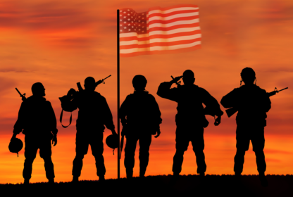 Silhouetted soldiers stand with weapons and salute in front of an American flag at sunset.