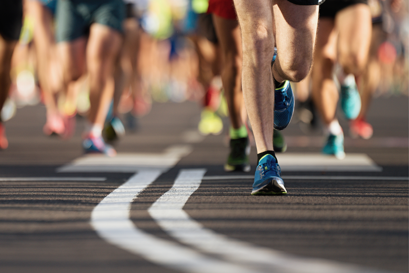 Close-up view of runners' legs and shoes on a road during a race.