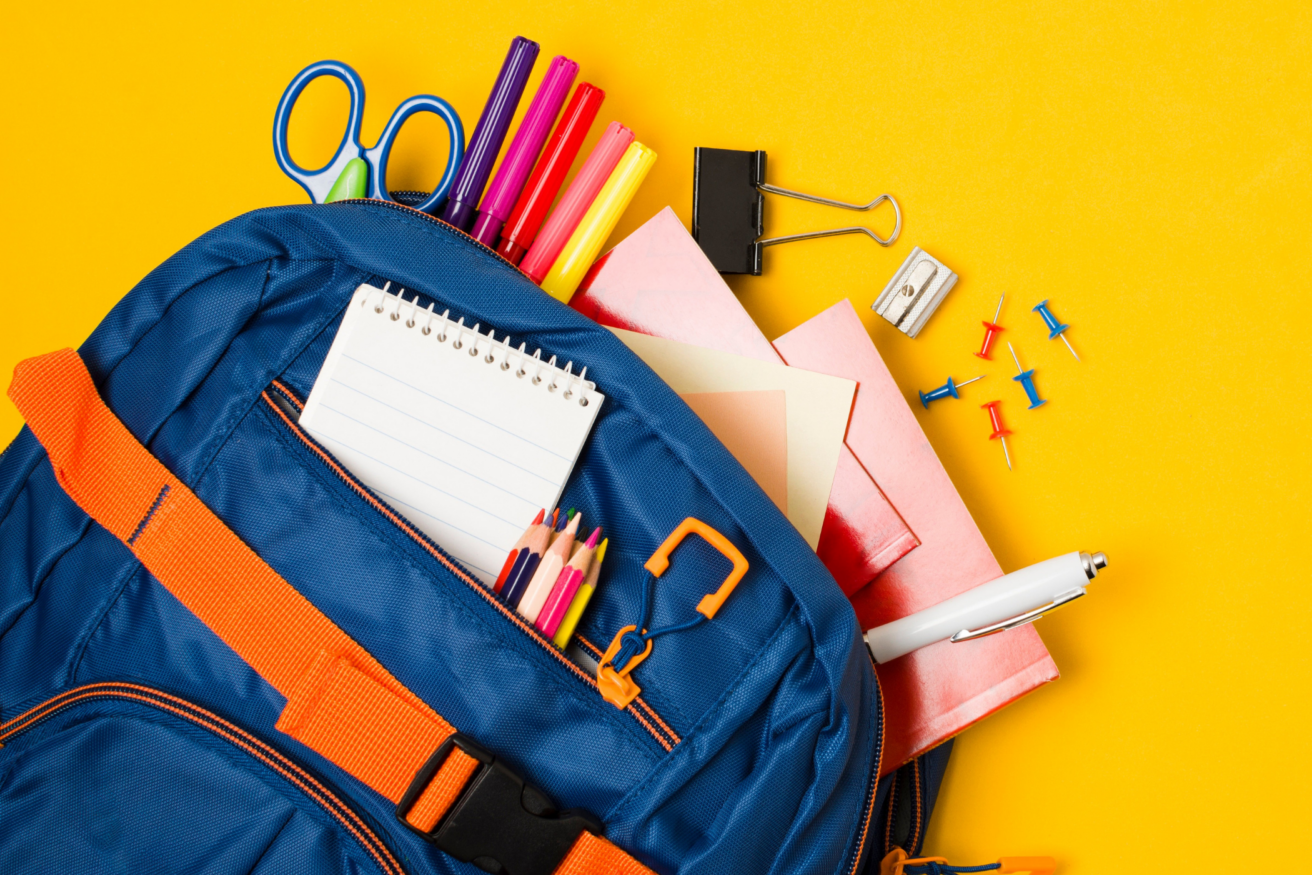 A blue backpack with orange accents contains colorful pens, a notepad, scissors, papers, a pen, a binder clip, a sharpener, and push pins, all set against a yellow background.