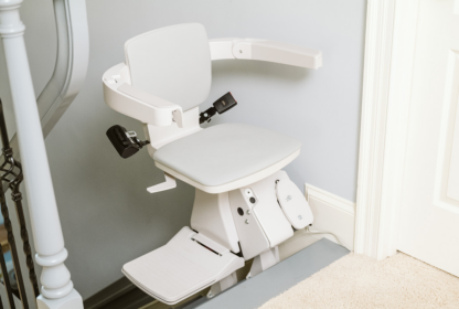 A stairlift is installed on a staircase, featuring a padded seat, backrest, and safety arms.