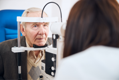 An elderly man is having his eyes examined using medical equipment by a healthcare professional in an eye clinic.