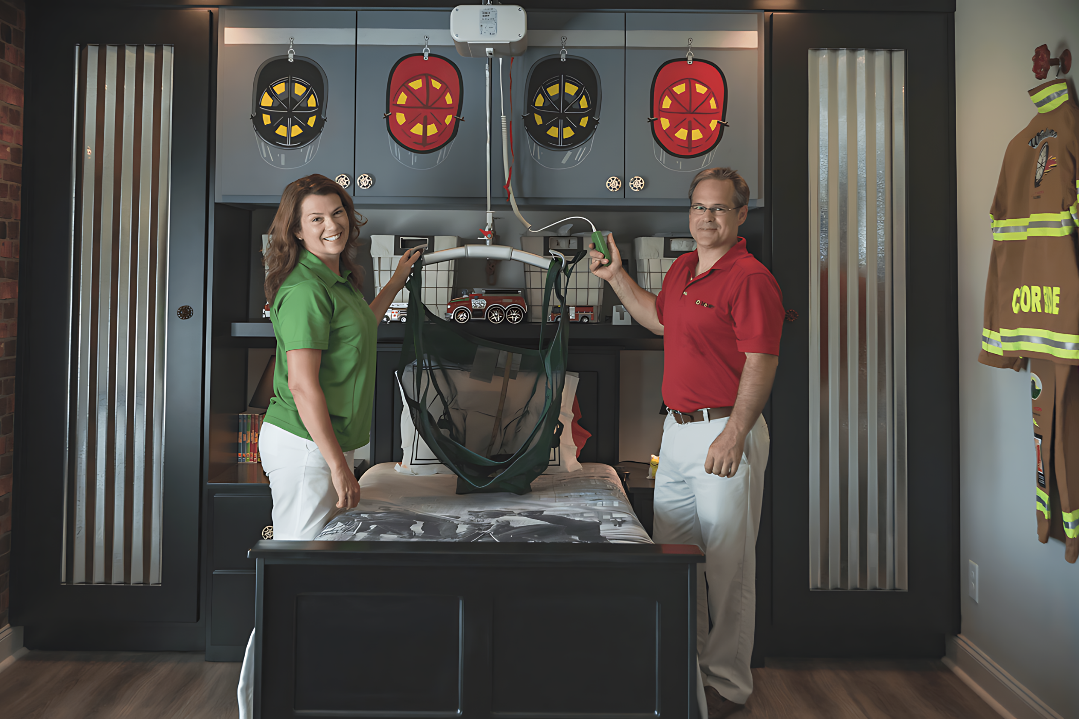 Two adults standing by a child's bed, holding a mobility assistive device. The room has firefighter-themed decorations, including helmets, a firetruck mural, and a hanging firefighter uniform.