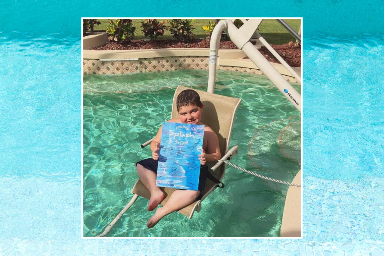 A child holding a book titled "Splash!" sits on a pool chair partially submerged in the water, with a hose attached to the chair. The background shows a pool and some plants.