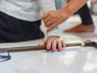 A person helps another who has fallen, with one hand on their arm and a cane and glasses on the floor nearby.