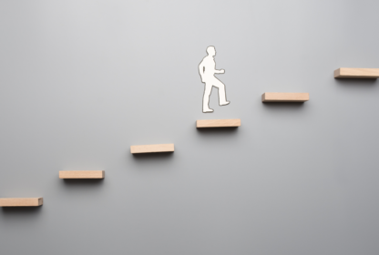 Silhouette of a person ascending a series of floating wooden steps against a plain gray background, symbolizing progress or personal growth.