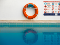 A life preserver hangs on a wall next to a pool rules sign above a swimming pool.