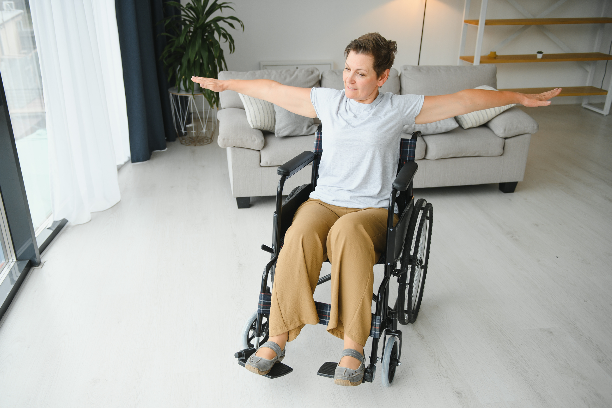 A person in a wheelchair exercises with arms extended in a living room.