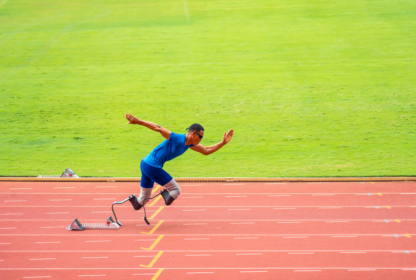 An athlete with prosthetic legs sprints on a red track, with green grass in the background.