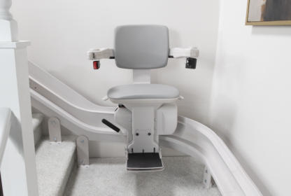 A gray stairlift is installed on a staircase with light-colored carpet, designed to assist individuals with mobility issues.