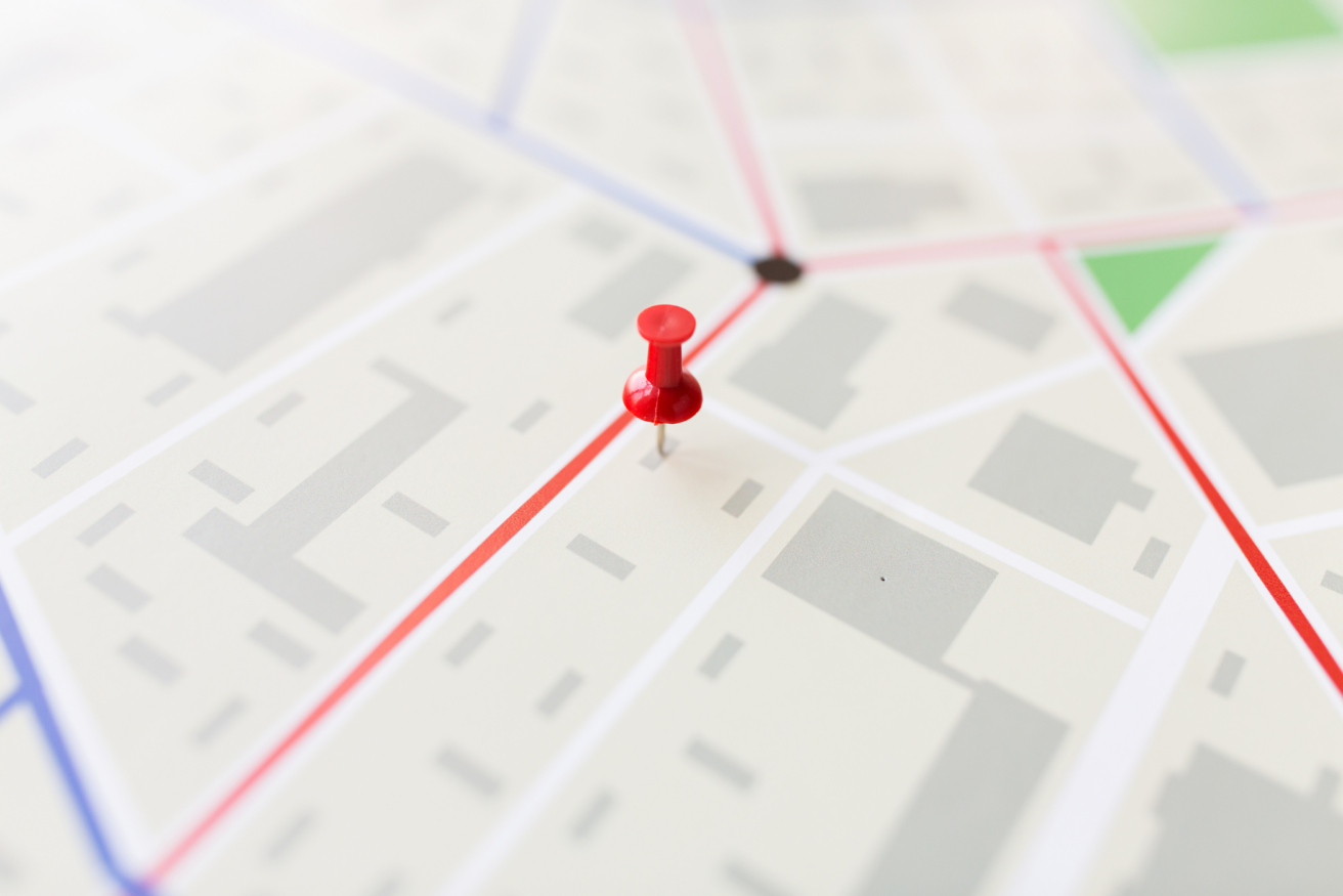 A red pushpin is placed on a map, marking a specific location. The map shows various streets and blocks in a light color scheme.