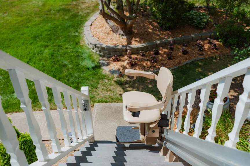 Outdoor stairlift on a residential staircase, leading down to a garden with a stone border and various plants.