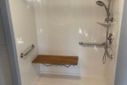 A shower stall with grab bars, a fold-down wooden seat, an adjustable showerhead, and a handheld showerhead.