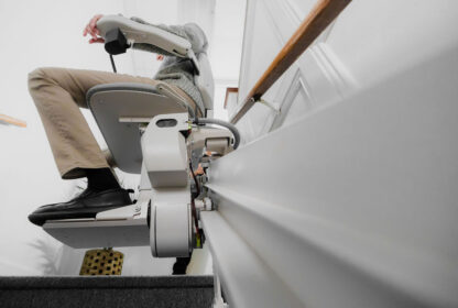 A person using a stairlift to ascend a staircase, showcasing the mechanism and rail attached to the stairs.