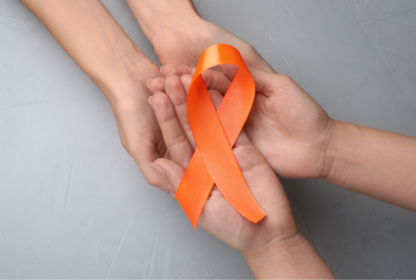 Two pairs of hands holding an orange awareness ribbon on a gray background.