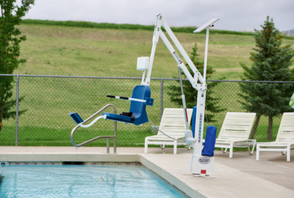 A pool lift at the edge of an outdoor swimming pool with lounge chairs and a green lawn in the background.