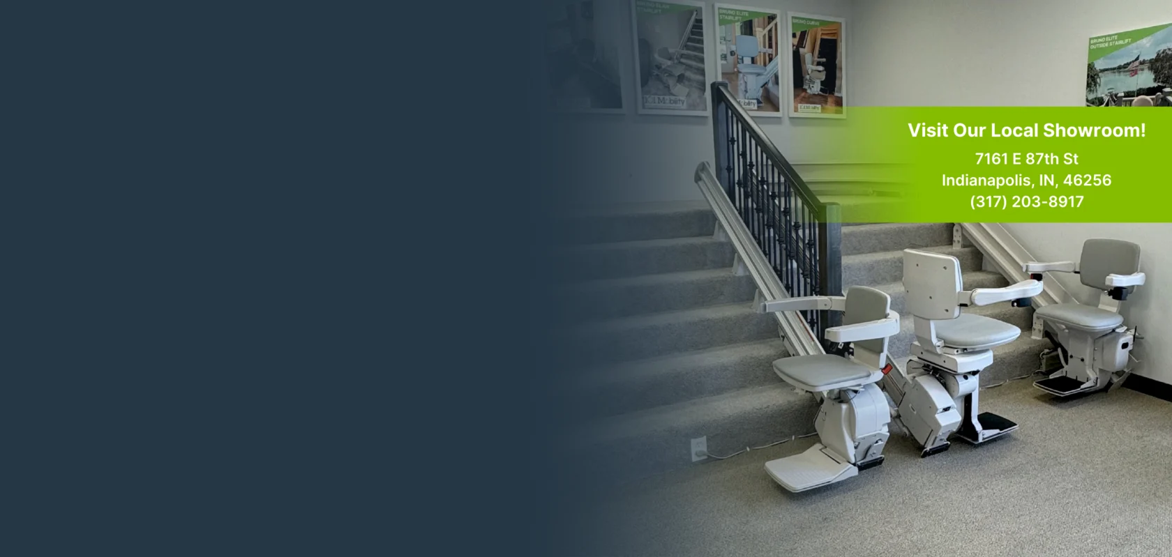 Two stairlifts next to a staircase in a showroom, with a green sign displaying the address and phone number for the local showroom in Indianapolis, IN.