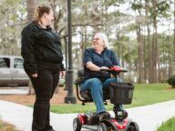 a person using a 4-wheel golden technologies power scooter in a park.