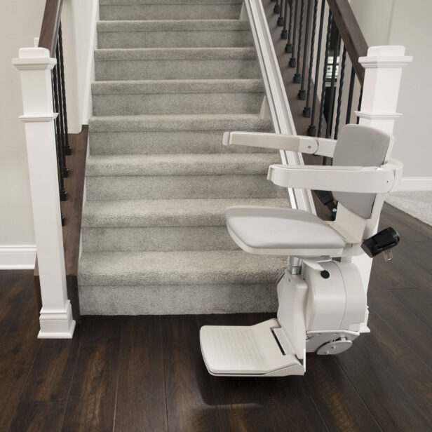 A stairlift installed next to a carpeted staircase with dark wooden steps and metal railings.