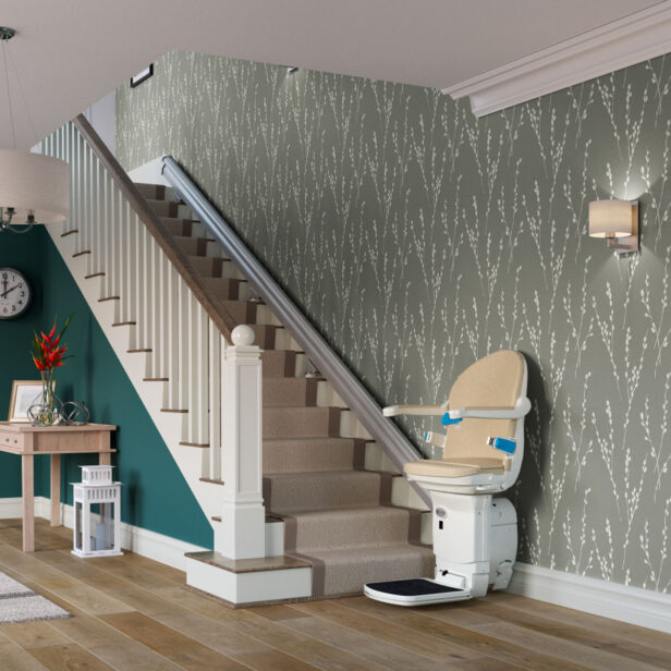 A stairlift is installed along a carpeted staircase in a modern home interior with patterned wallpaper, a clock, a small table, and a light fixture.