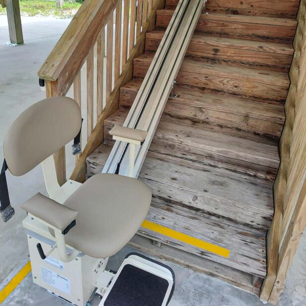 Image of a stair lift installed beside a wooden staircase, intended for assisting individuals with mobility difficulties to ascend and descend the stairs.