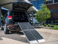 An open black SUV with a ramp extending from the trunk to the ground outside a modern building.