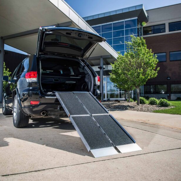 An open black SUV with a ramp extending from the trunk to the ground outside a modern building.