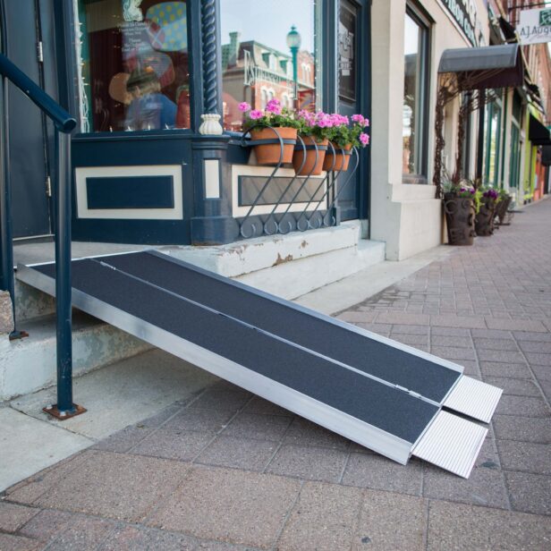 A portable ramp provides wheelchair access to a storefront with steps. The ramp leads from the sidewalk to the entrance, which is decorated with potted flowers.