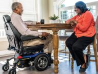 a person using a blue pride power chair in a kitchen.