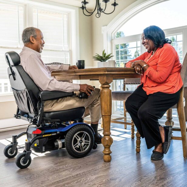 a person using a blue pride power chair in a kitchen.