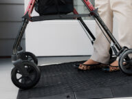 Person using a walking aid with a black mat underfoot near a door.