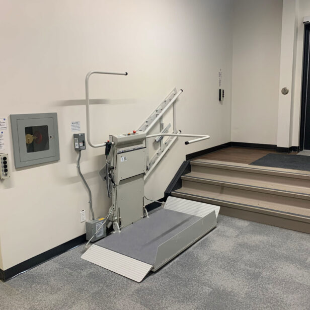 A motorized wheelchair lift positioned beside a short staircase within a building, providing access between two different floor levels.