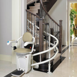 A stairlift is installed on a curved staircase in a modern home, featuring a padded seat, armrests, and footrest, designed to assist individuals with mobility challenges.