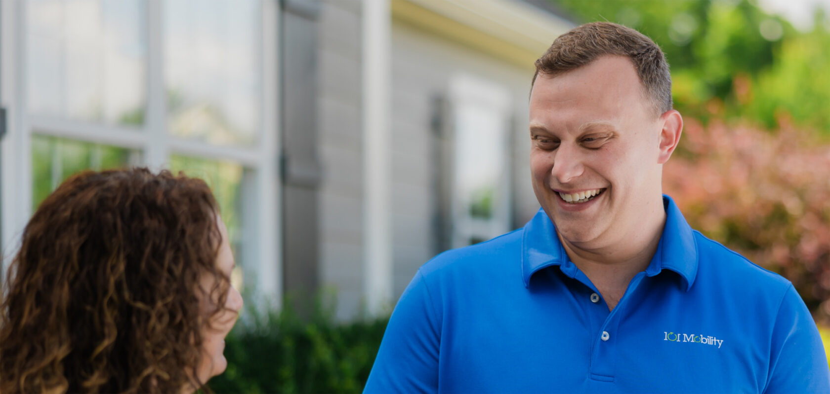 Two people are conversing outdoors; one is wearing a blue polo shirt with a logo, and they are both smiling.