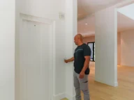 A man stands in a modern, brightly lit hallway, pressing a button to call an elevator.