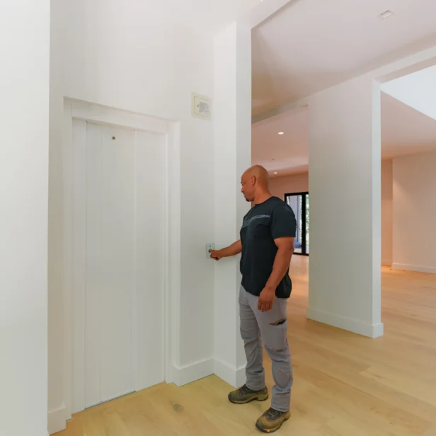 A man stands in a modern, brightly lit hallway, pressing a button to call an elevator.