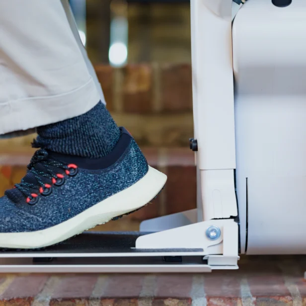 A person wearing blue sneakers and beige pants is using a stairlift, descending a brick staircase.