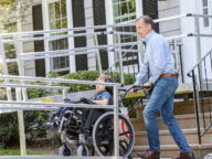 a parent pushing their child on a wheelchair up an aluminum ramp.